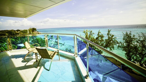 A balcony with a glass railing overlooking a pool and the ocean.