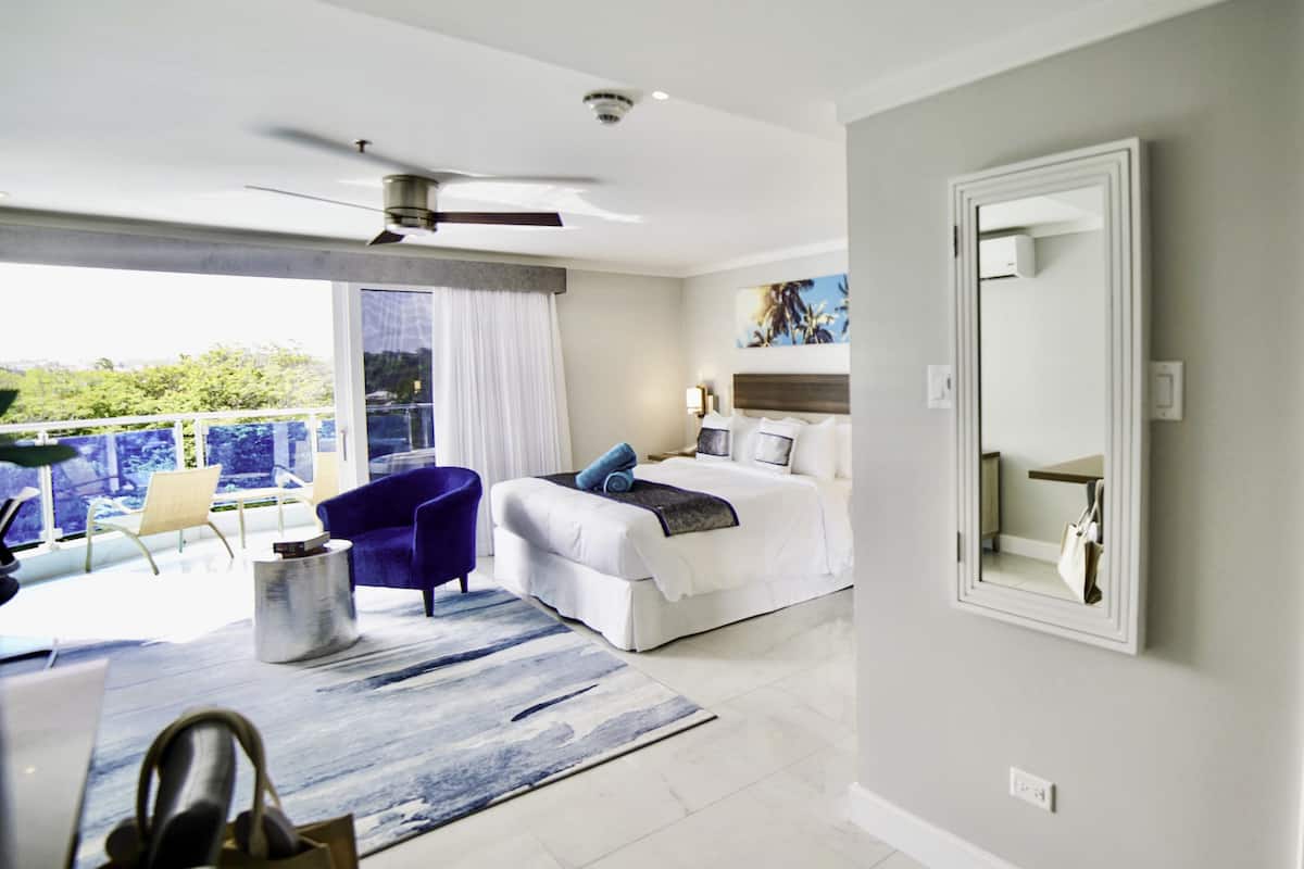 Une chambre d’hôtel moderne dotée d’un balcon, d’un lit, d’une chaise, d’un bureau et d’un grand miroir.