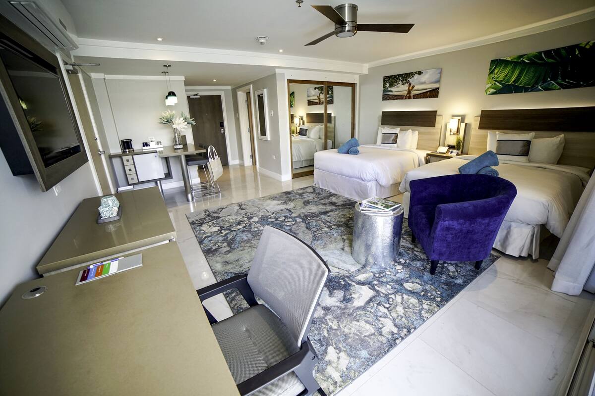Une chambre d’hôtel équipée d’un lit, d’un bureau, d’une chaise, d’une télévision et d’un ventilateur de plafond.