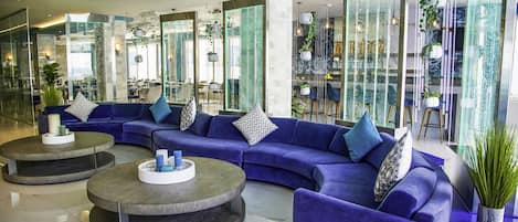 A modern lobby with a blue sectional sofa, two round coffee tables, and a glass partition.