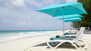 A beach with white lounge chairs and turquoise umbrellas, a clear sky, and the ocean in the background.