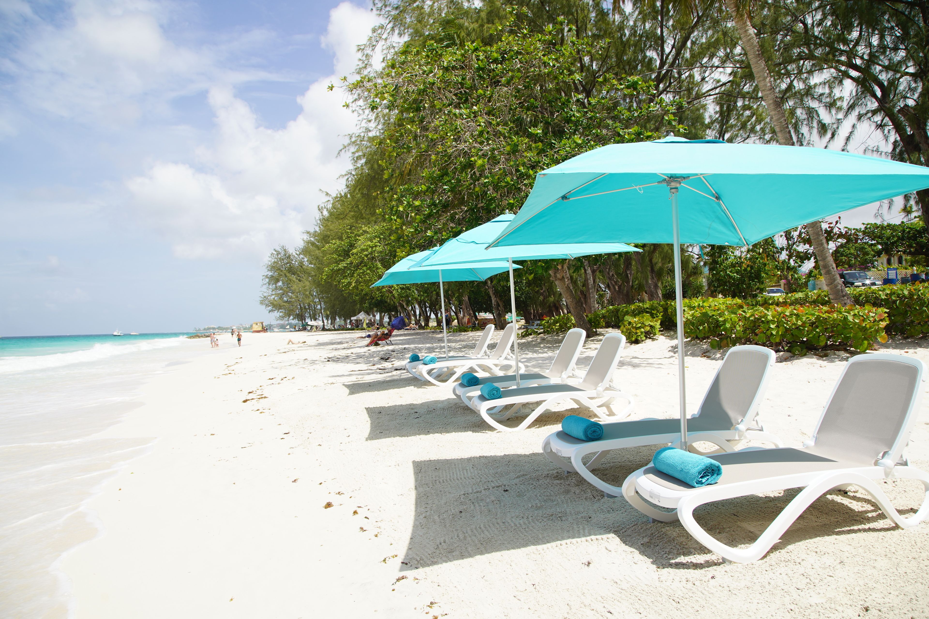 Une plage avec des chaises longues blanches et des parasols turquoise, alignés le long du rivage.