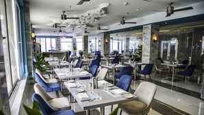 A modern restaurant with multiple dining tables and chairs, large windows, and ceiling fans.