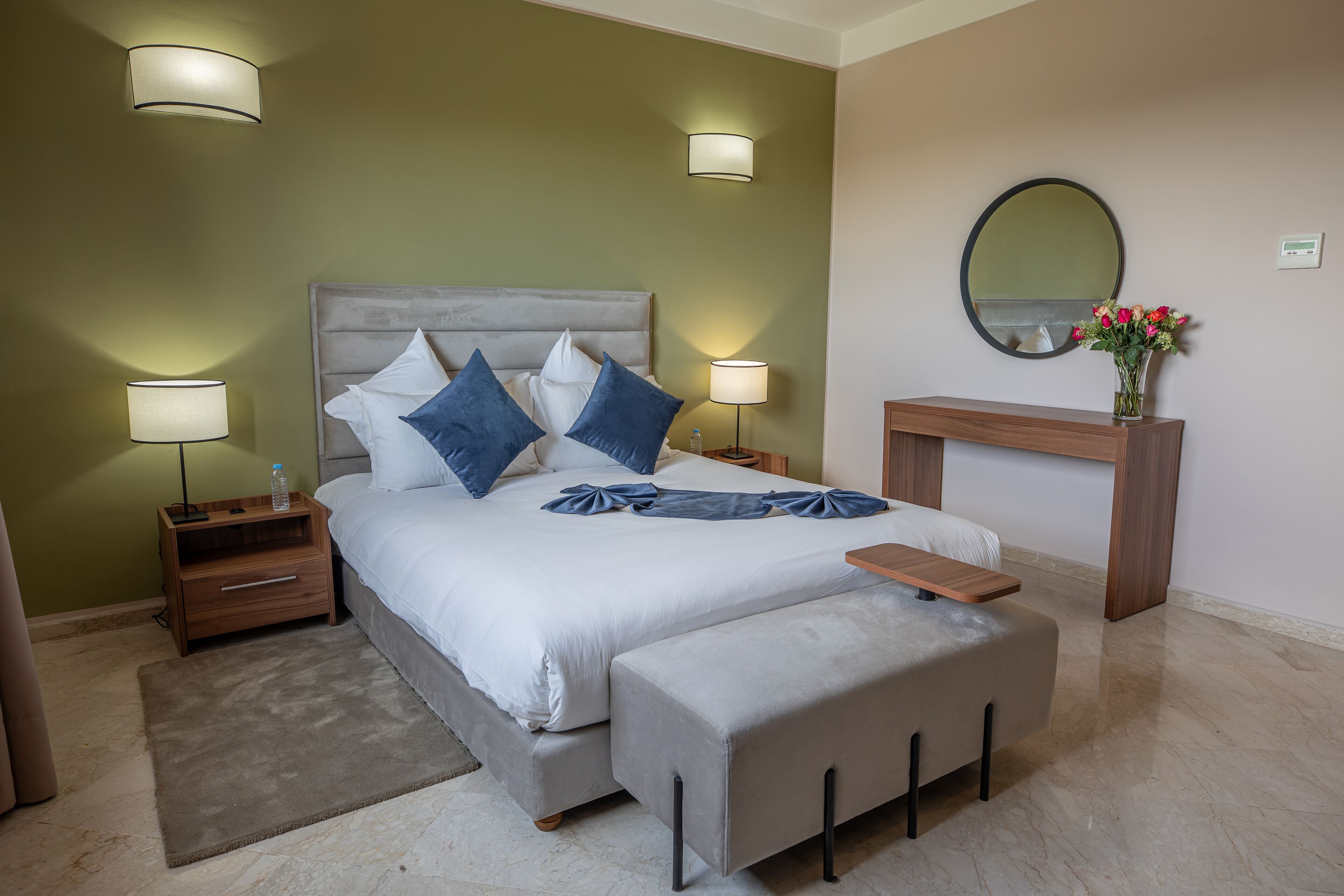 Une chambre à coucher avec un lit, des tables de chevet, des lampes, un miroir et un vase avec des fleurs.