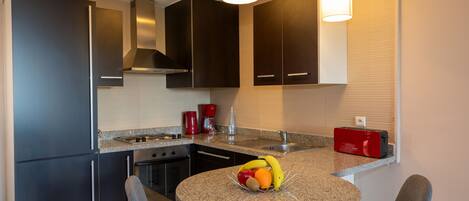 A modern kitchen with dark cabinets, a granite countertop, a round table with two chairs, a fruit bowl, and a red toaster.