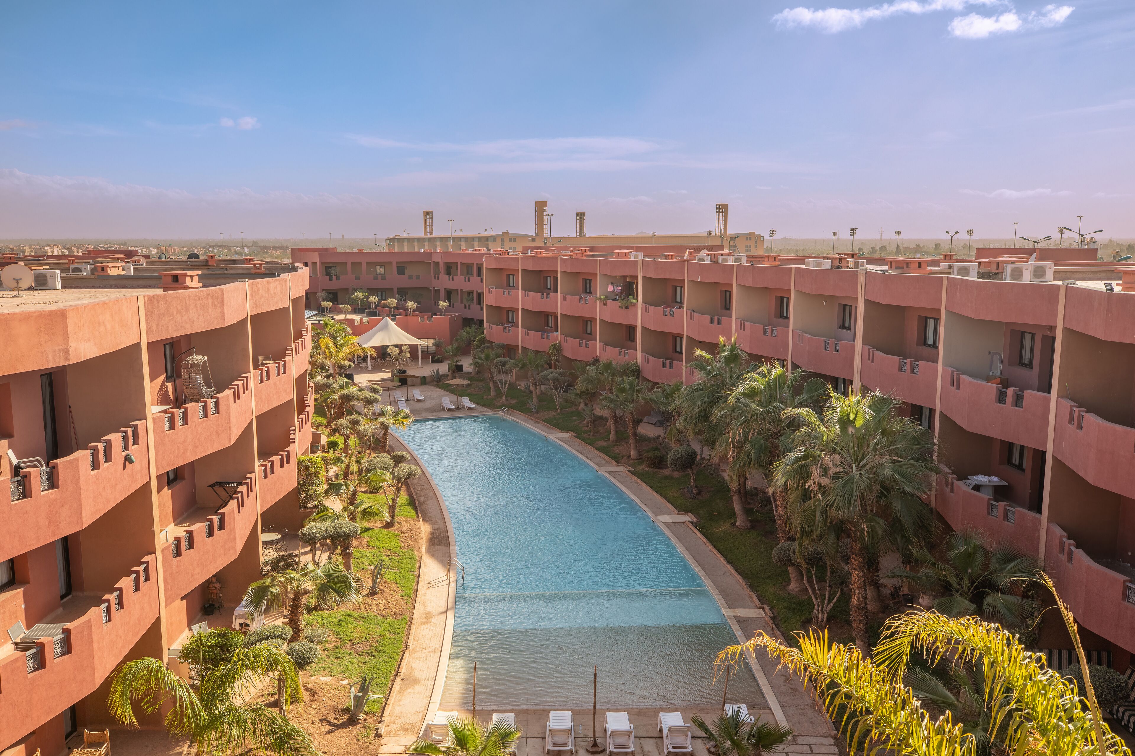 Un hotel con piscina rodeada de palmeras y sillas de descanso.