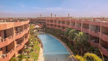 A hotel with a swimming pool surrounded by palm trees and lounge chairs.