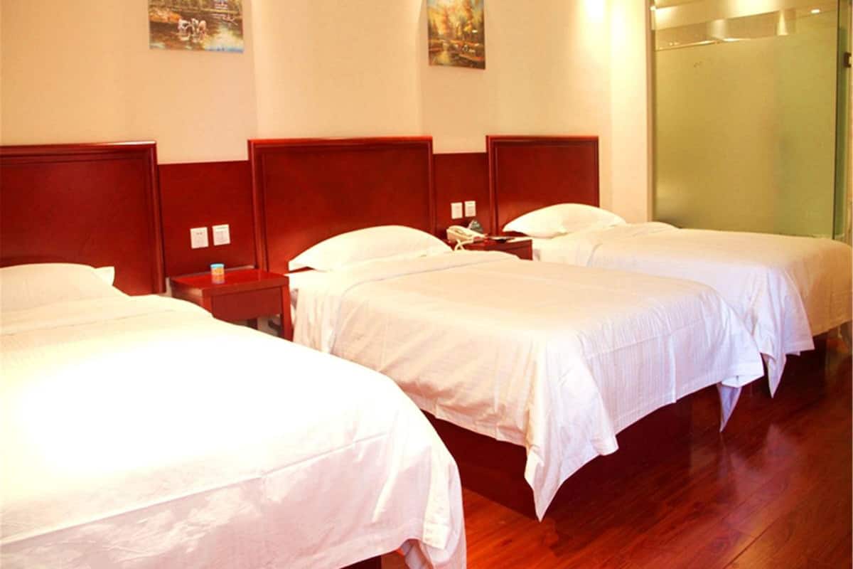 A hotel room with three single beds, wooden headboards, white bedding, and a glass door.