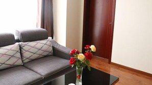 Een woonkamer met een grijze bank, een glazen salontafel en een vaas met bloemen.
