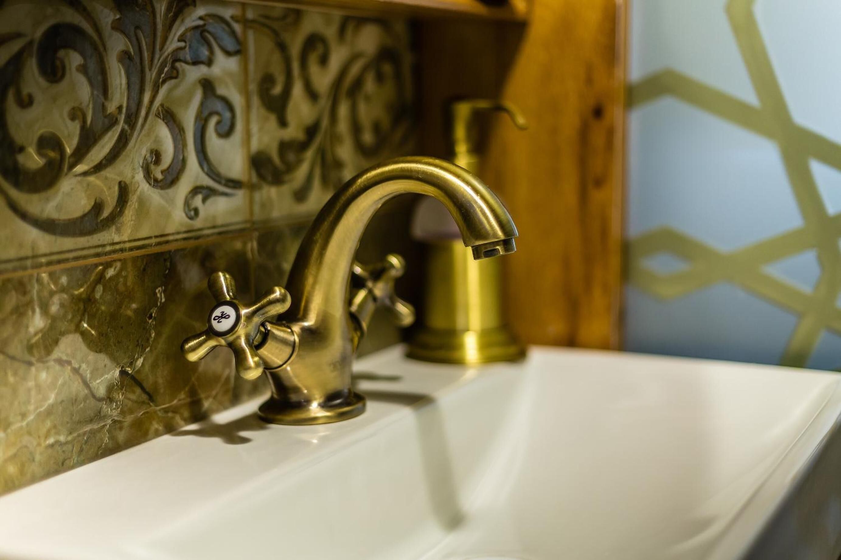 A bathroom with a gold faucet, a white sink, and decorative tiles.