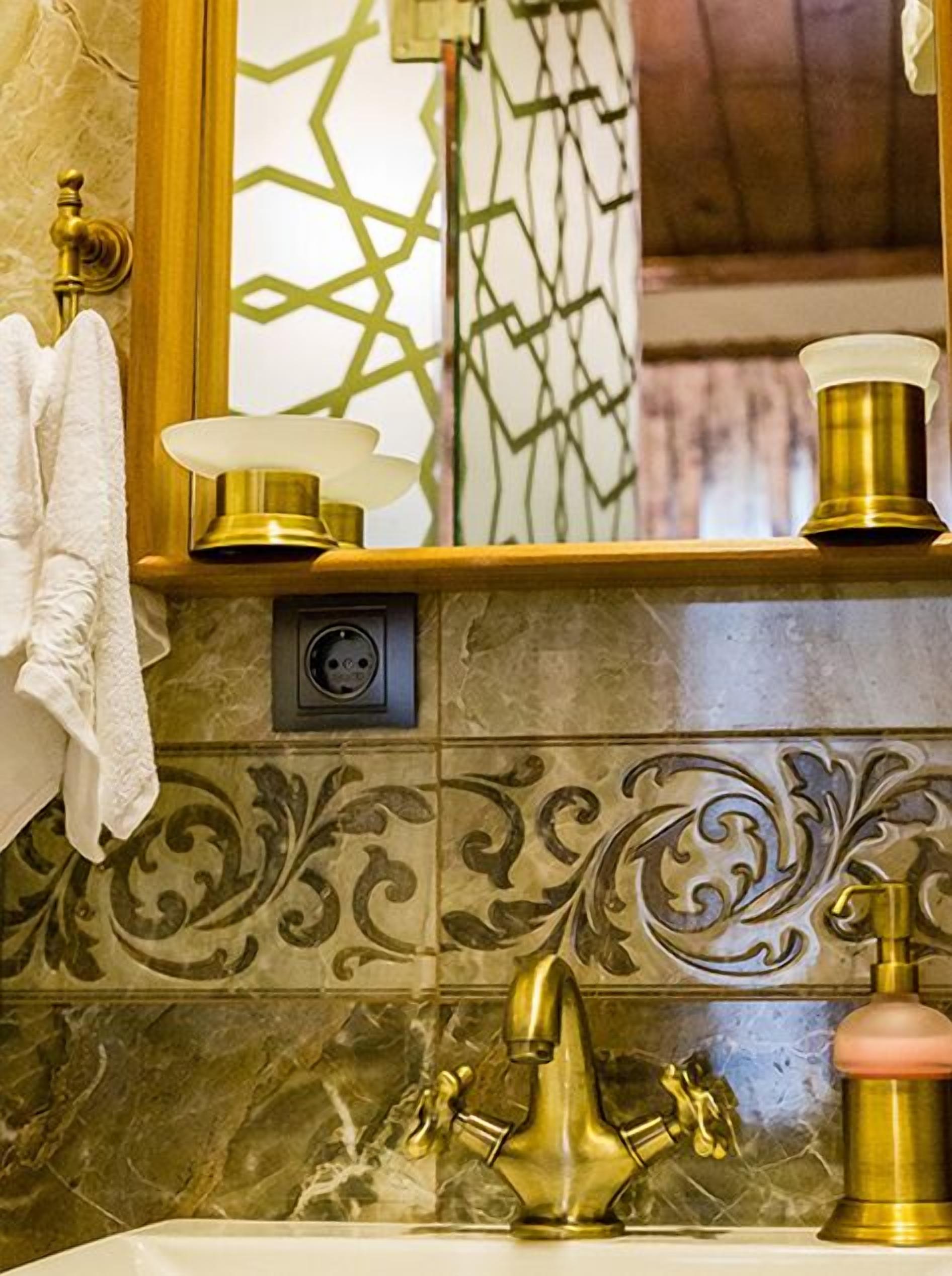 A bathroom with a gold faucet, a towel hanging on the wall, and a mirror with a geometric pattern.