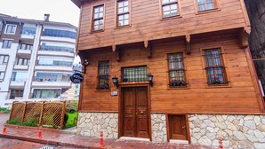 A wooden building with a stone base, a large wooden door, and multiple windows. - Kum Pansiyon  (Amasra)