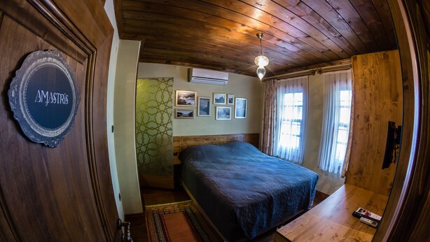 A wooden-paneled room with a bed, a desk, and a wall-mounted air conditioner. - Kum Pansiyon  (Amasra)