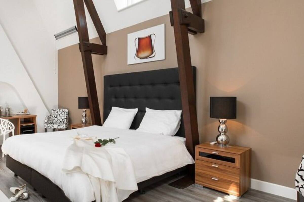 A bedroom with a large bed, a bedside table, a nightstand, a chair, a bathtub, and a mirror.