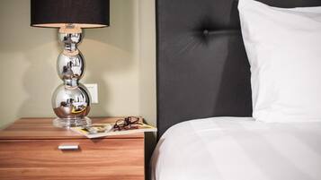 A neatly made bed with white linens, a dark headboard, a wooden nightstand with a lamp, and a magazine.