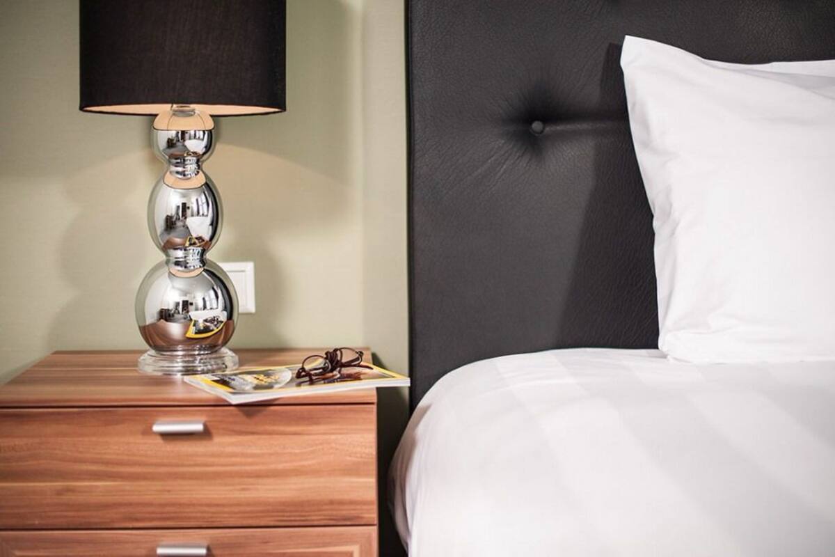 A neatly made bed with a black headboard, a wooden nightstand with a lamp, and a magazine.
