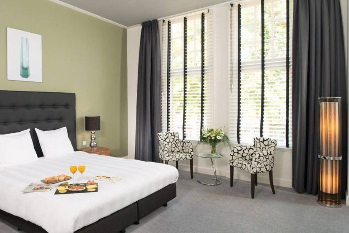 A hotel room with a large bed, two bedside tables, a nightstand, a chair, a table with flowers, and a floor lamp.