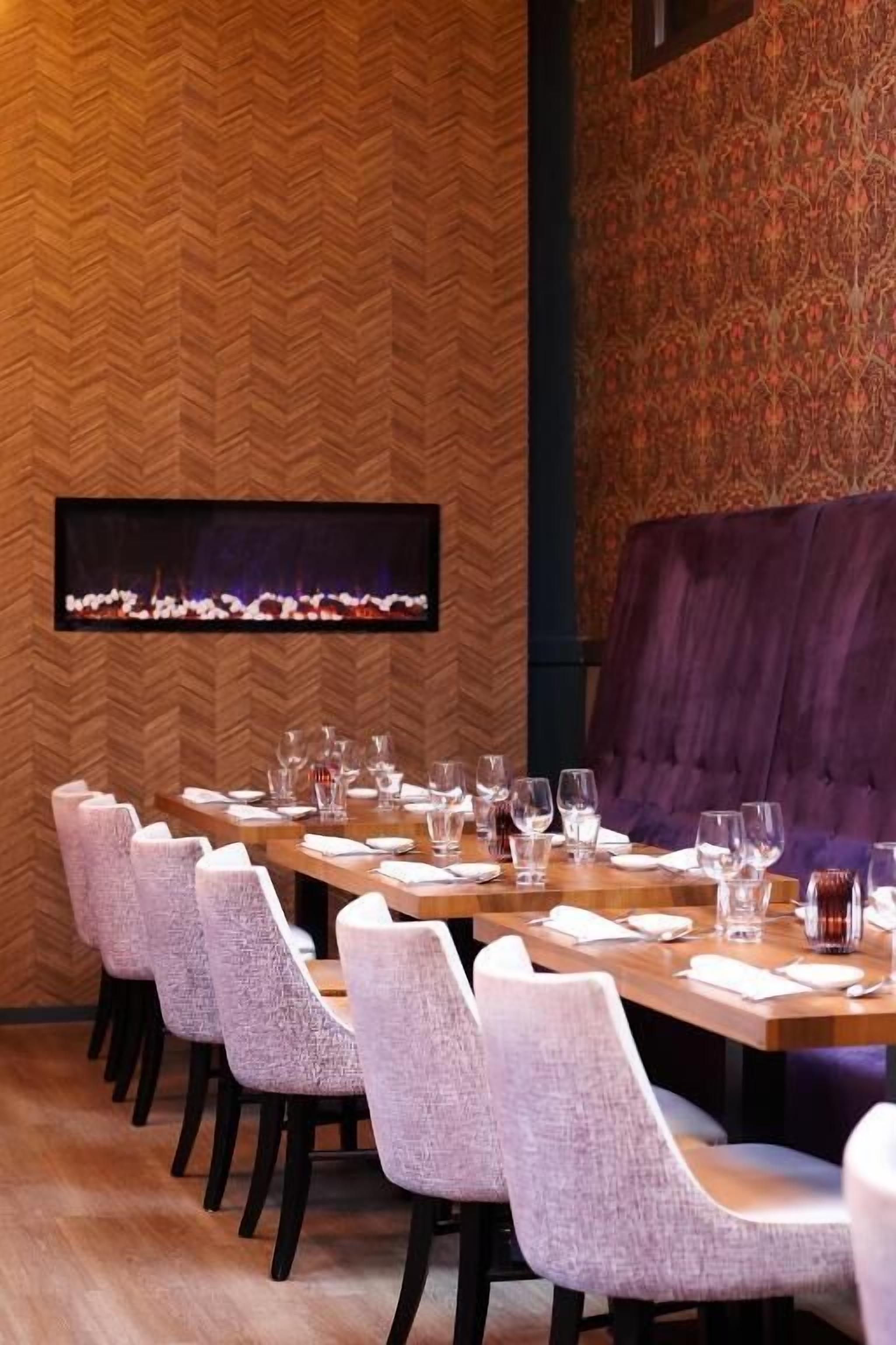 A dining area with a long table set for multiple guests, chairs, and a fireplace.
