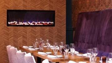 A dining area with a long table set for multiple guests, chairs, and a fireplace.