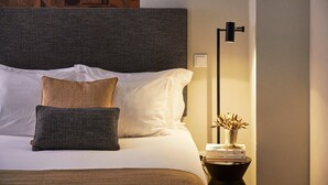 Un lit bien fait, avec une literie blanche et marron, une tête de lit à motifs et une table de chevet sur laquelle se trouvent une lampe et un vase de fleurs.