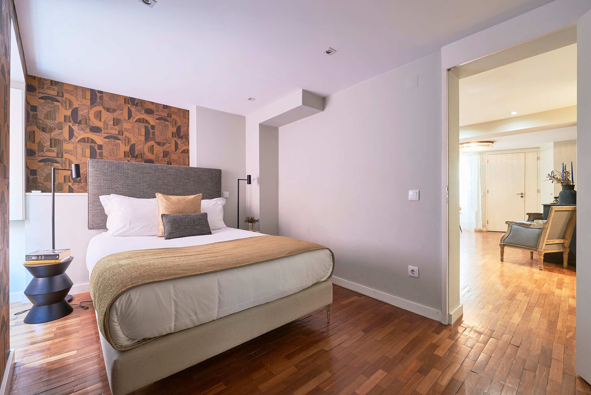 Un dormitorio moderno con una cama grande, suelo de madera y un papel tapiz estampado.
