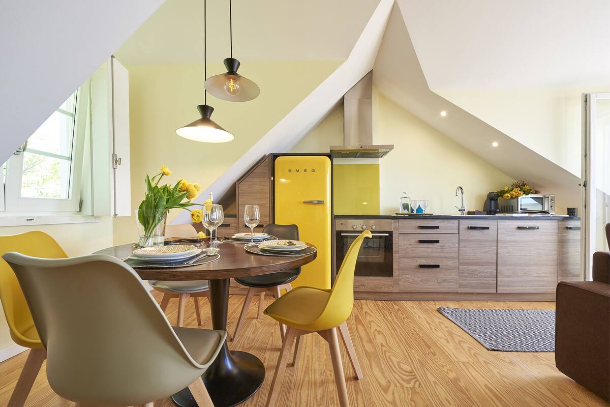 A modern kitchen with a yellow refrigerator, wooden cabinets, and a dining area with a round table and chairs.