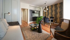 Un salon moderne avec un canapé, une table basse agrémentée de livres et d’une plante, un coin repas avec des chaises, et une cuisine en arrière-plan.