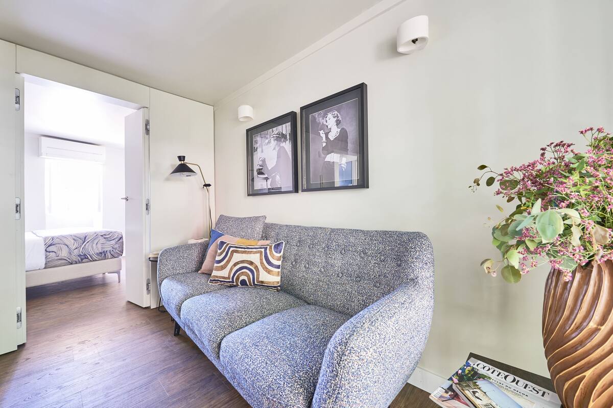 A modern living room with a grey sofa, a small table, a floor lamp, and a framed picture on the wall.