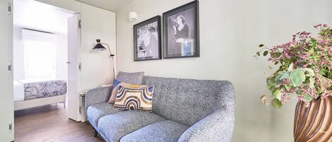 A modern living room with a grey sofa, a small table, a floor lamp, and a framed picture on the wall.