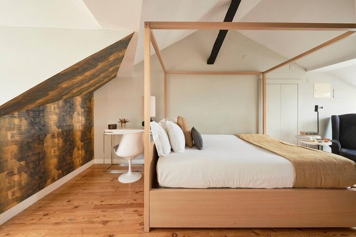 A bedroom with a wooden four-poster bed, a desk with a chair, and a modern lamp.