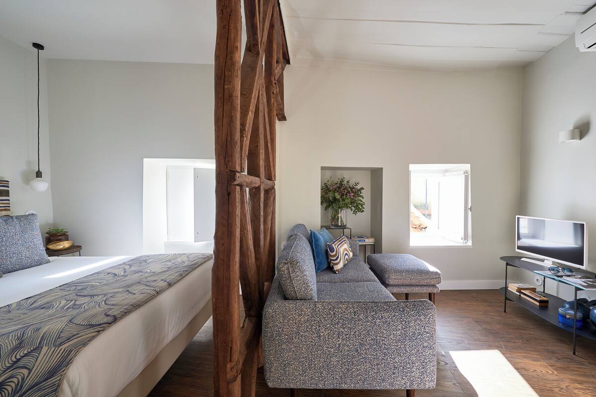 A bedroom with a bed, a sofa, a TV, and a wooden structure.