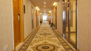 A hotel hallway with a patterned carpet, wooden doors, and a glass elevator. - GreenTree Inn ZhuHai Jinwan District Zhuhai Airport Jilin University Hotel (Zhuhai)