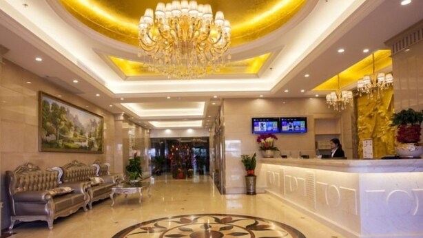 A hotel lobby with a reception desk, a chandelier, and a large painting on the wall. - GreenTree Inn ZhuHai Jinwan District Zhuhai Airport Jilin University Hotel (Zhuhai)