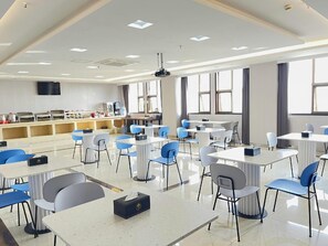Een klaslokaal met tafels en stoelen, een beamer en een televisie aan de muur.