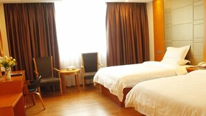A hotel room with two beds, a desk with a chair, a small table, and a vase with flowers. - Greentree Inn Shantou Dahao (Yingtan)
