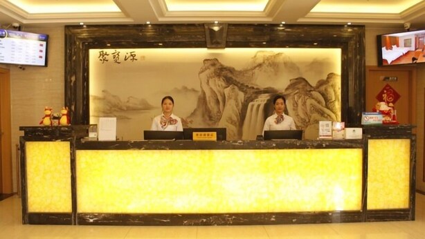 A reception desk with two staff members, a large mural, and a television screen. - Greentree Inn Shantou Dahao (Yingtan)