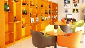 A modern hotel lobby with a vibrant orange shelving unit displaying various decorative items. There are several seating areas with colorful chairs and a small table. - Greentree Inn Shantou Dahao (Yingtan)