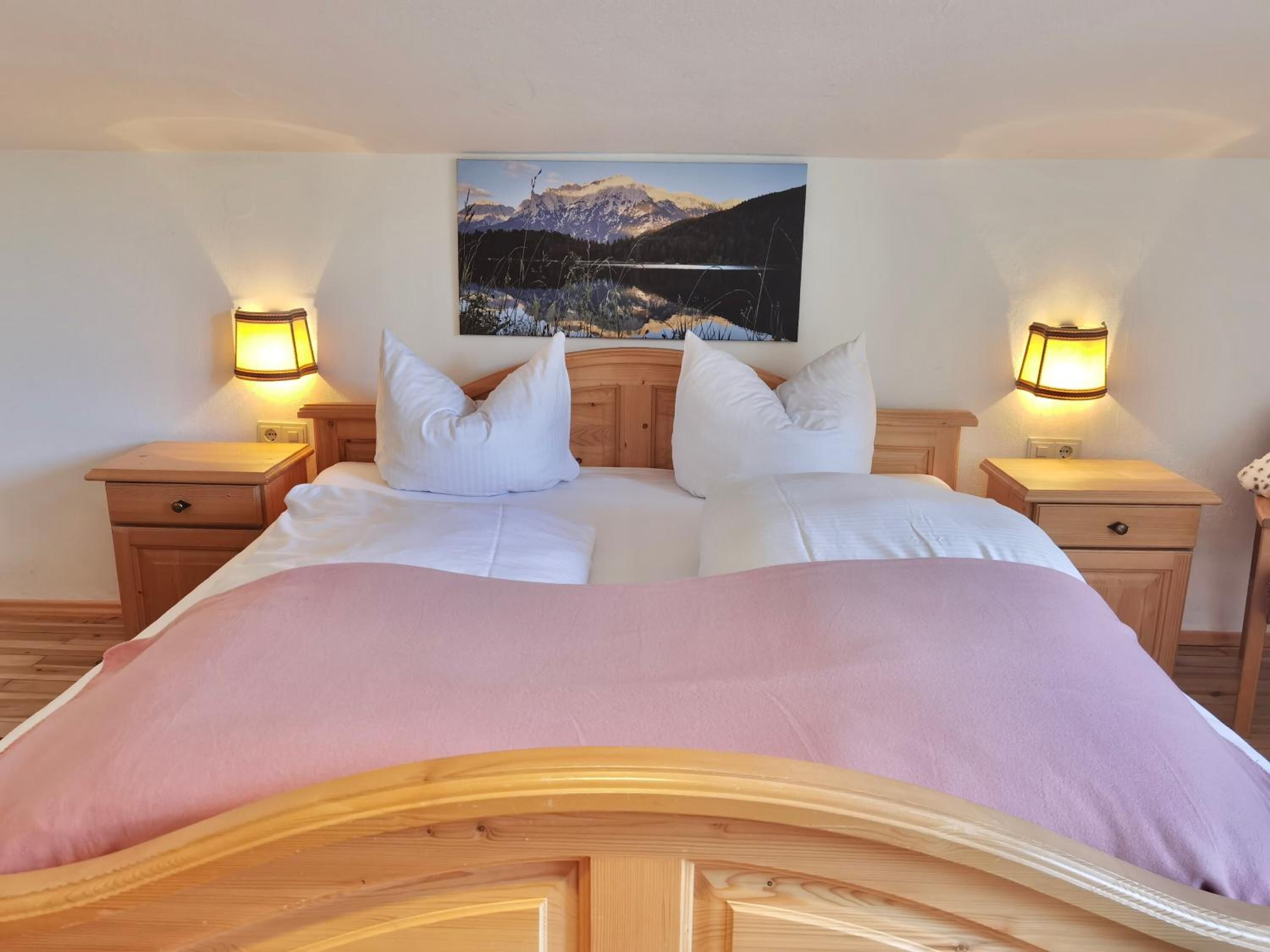 Un letto matrimoniale con testiera in legno, due comodini con lampade e un quadro che raffigura un paesaggio montano sopra il letto.