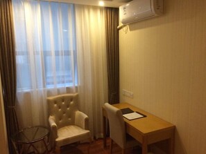 A hotel room with a wooden desk, a tufted armchair, and a small round table. - GreenTree Inn Zhuhai Light Rail Pearl Station Express Hotel (Zhuhai)