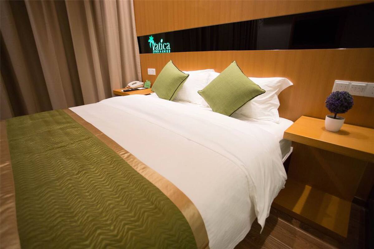 Habitación de hotel con cama, almohadas verdes, mesita de noche y un cartel que dice 'Vatica'.