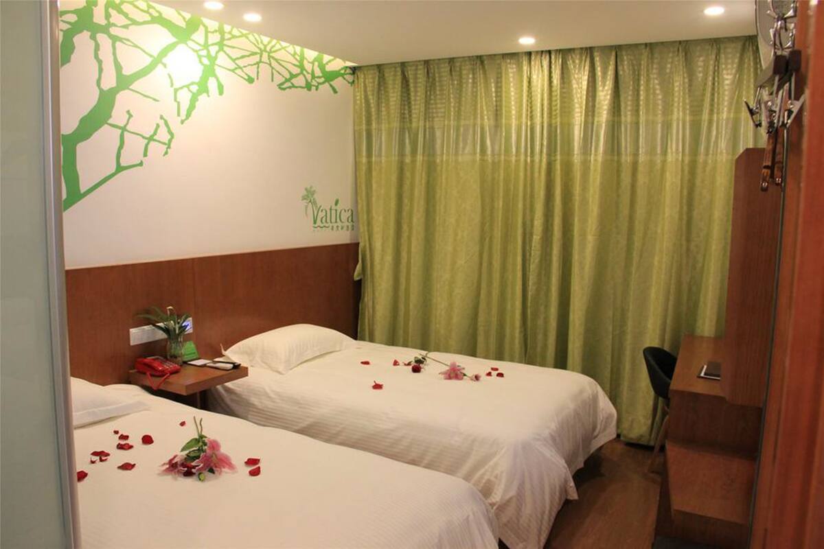 Habitación de hotel con dos camas, cabecero de madera, escritorio y cortina verde.