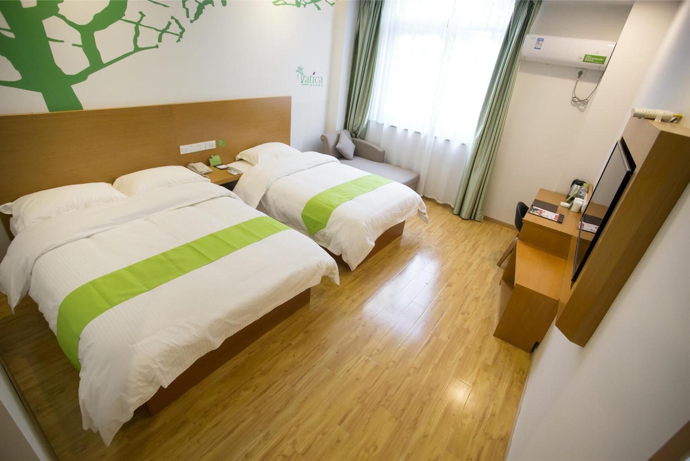 A hotel room with two beds, a wooden floor, a desk, a chair, a TV, and a window with curtains.
