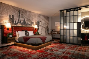 A modern bedroom with a cityscape mural, a red and black patterned carpet, and a large bed with a wooden frame. - The Nash (Nashville)