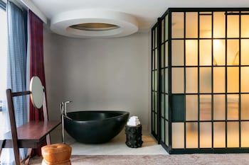 Relax in a serene bathroom with a large bathtub, wooden chair, and round mirror. at Bobby Hotel