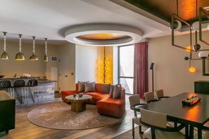 Una sala de estar moderna con un sofá seccional, una mesa de centro redonda y una zona de comedor con una mesa y sillas oscuras.