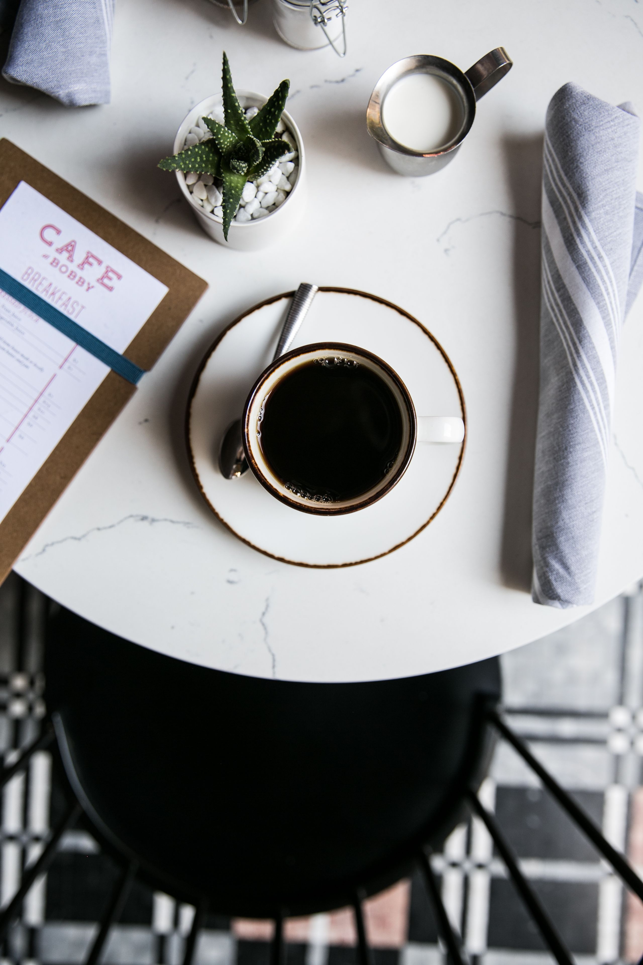 A round table with a coffee cup, a menu, a small potted plant, and a napkin.