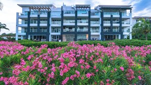 Een hotel met meerdere verdiepingen, balkons, een tuin met roze bloemen en een heldere lucht.