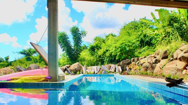 Une piscine aux eaux d’un bleu limpide, dont le fond est recouvert de carreaux, entourée de rochers et de verdure.