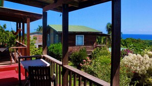 Une terrasse en bois avec une table et des chaises, d’où l’on peut admirer une maison dotée d’un toit végétalisé et une vue sur l’océan.