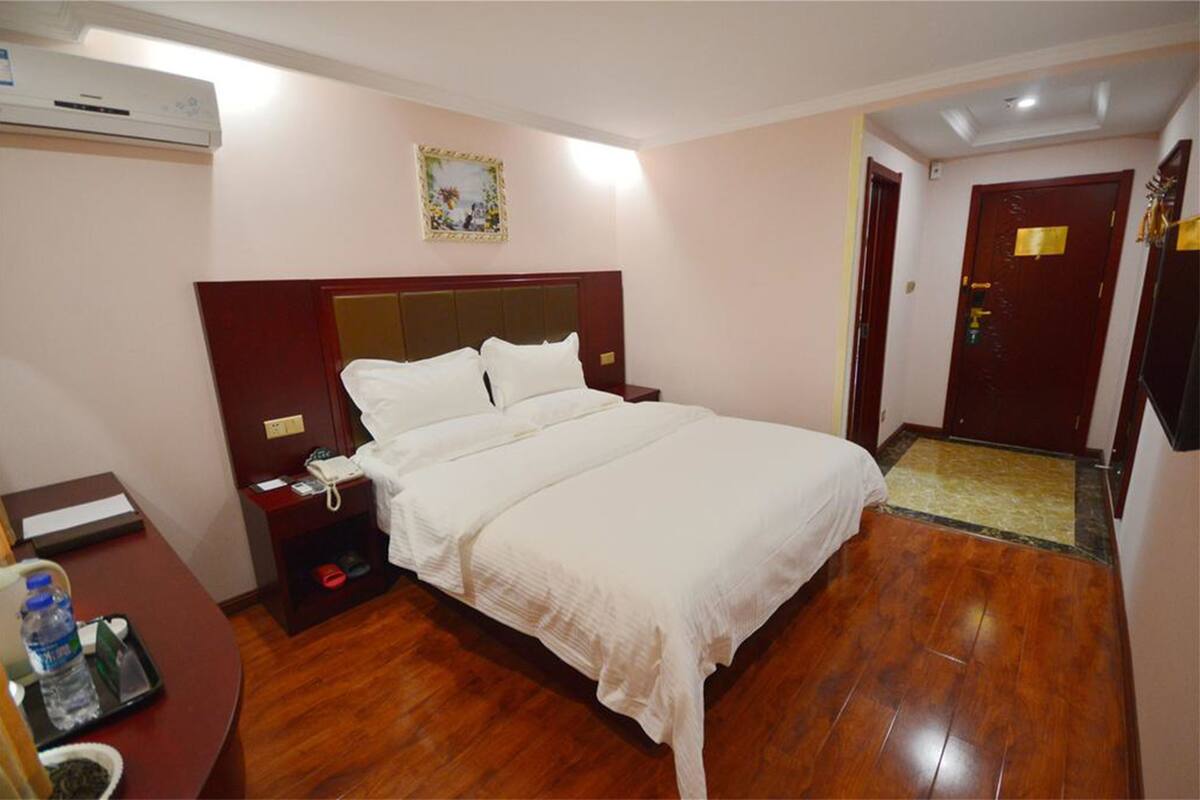 Une chambre d’hôtel avec un grand lit, une table de chevet avec une lampe, un bureau avec une chaise et une porte avec une poignée.